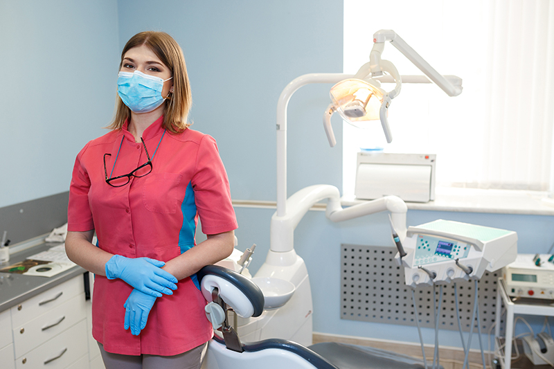 girl dentist stands in the middle of their equipment and looking at the camera